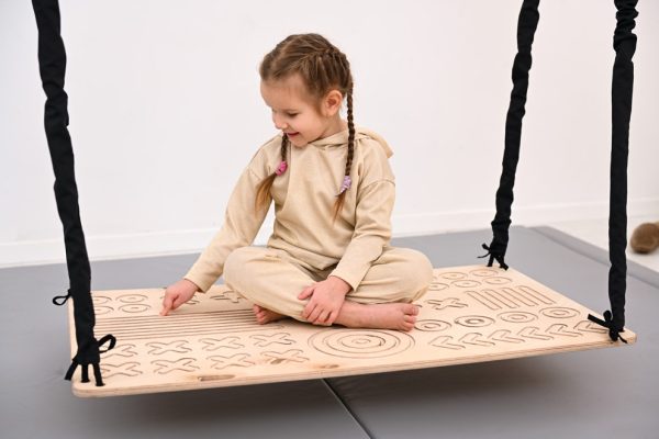 Dziewczynka siedzi na wiszącej platformie sensorycznej Good Wood