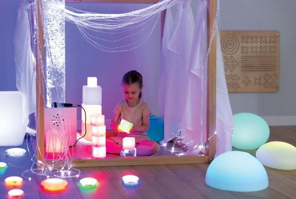 Dziecko siedzące w sensorycznym kąciku z kolorowymi, świecącymi zabawkami i elementami świetlnymi.