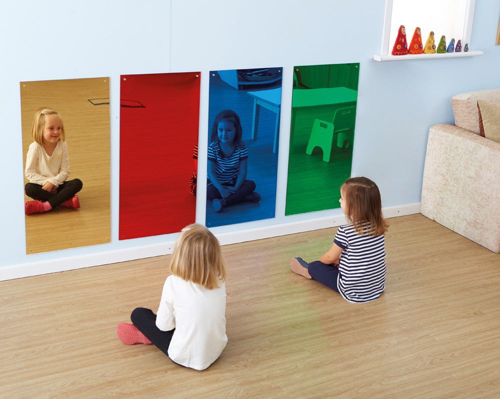 Dziewczynki siedzące przed kolorowymi panelami lustrzanymi, obserwujące swoje odbicia w różnych barwach.