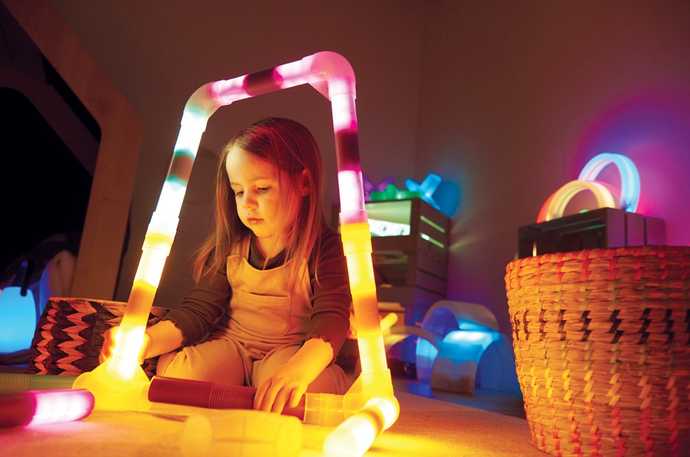 Dziewczynka bawiąca się kolorowymi, świecącymi rurkami w sensorycznym kąciku.